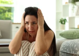 woman sitting on the floor with her hands on her head, expressing feelings of anxiety and distress.
